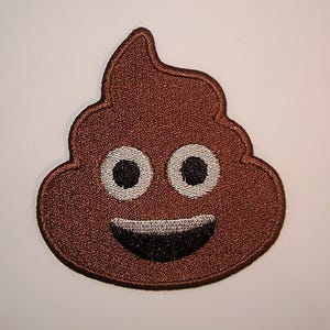 May include: A brown embroidered patch in the shape of a smiling poop emoji. The patch has white eyes with black pupils and a smiling mouth. A fun and playful accessory.