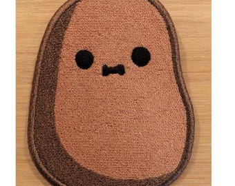 May include: An embroidered patch shaped like a potato with a light brown textured surface, a darker brown border, and a simple face featuring two small black circular eyes and a small black mouth centered in the middle of the oval-shaped design.