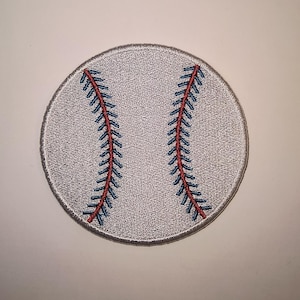 May include: Embroidered baseball patch with a grey background and red and blue stitching. The round patch has a textured surface, resembling a baseball.