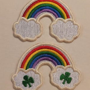 May include: Two embroidered rainbow patches with a white cloud base. The rainbows feature red, orange, yellow, green, blue, and purple arches. One patch has two green shamrocks on the cloud.