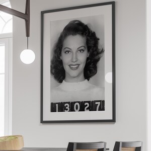 May include: Black and white photograph of a woman with dark hair, wearing a white shirt. The photo is framed in black and has the number "13027" printed at the bottom.