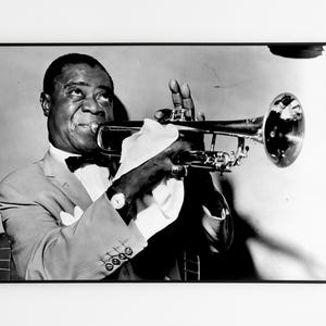 May include: A black and white photograph of a man playing a trumpet. He is wearing a suit and a bow tie. The trumpet is held in his right hand and he is looking up at the camera.
