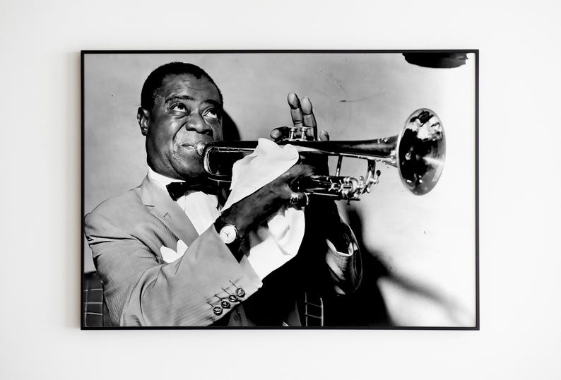 May include: A black and white photograph of a man playing a trumpet. He is wearing a suit and a bow tie. The trumpet is held in his right hand and he is looking up at the camera.
