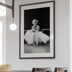 May include: Black and white photograph of a woman wearing a white tulle skirt and sitting on a chair. The woman is looking at the camera and smiling.
