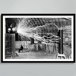 Puede incluir: Fotografía enmarcada en blanco y negro de un hombre sentado cerca de un experimento con una bobina de Tesla. La bobina emite potentes descargas eléctricas, creando una dramática exhibición de energía. La imagen captura la esencia de la exploración científica.