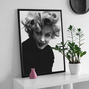Peut inclure: Photographie en noir et blanc encadr&eacute;e d'une femme aux cheveux blonds regardant l'appareil photo. La femme porte une chemise noire et a une expression s&eacute;rieuse sur son visage.