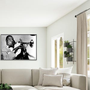 May include: Black and white photograph of a man playing a trumpet. The man is wearing a suit and bow tie. The photograph is framed in a black frame.