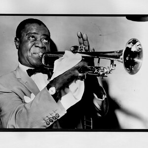 May include: A black and white photograph of a man playing a trumpet. He is wearing a suit and a bow tie. The trumpet is held in his right hand and the bell of the trumpet is pointed towards the right side of the image.