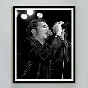 May include: Black and white photo of a man singing into a microphone. He is wearing a leather jacket and has a goatee.