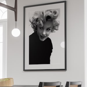 Peut inclure: Photographie en noir et blanc d'une femme aux cheveux courts et boucl&eacute;s. Elle regarde la cam&eacute;ra et sourit. La photo est encadr&eacute;e dans un cadre noir.