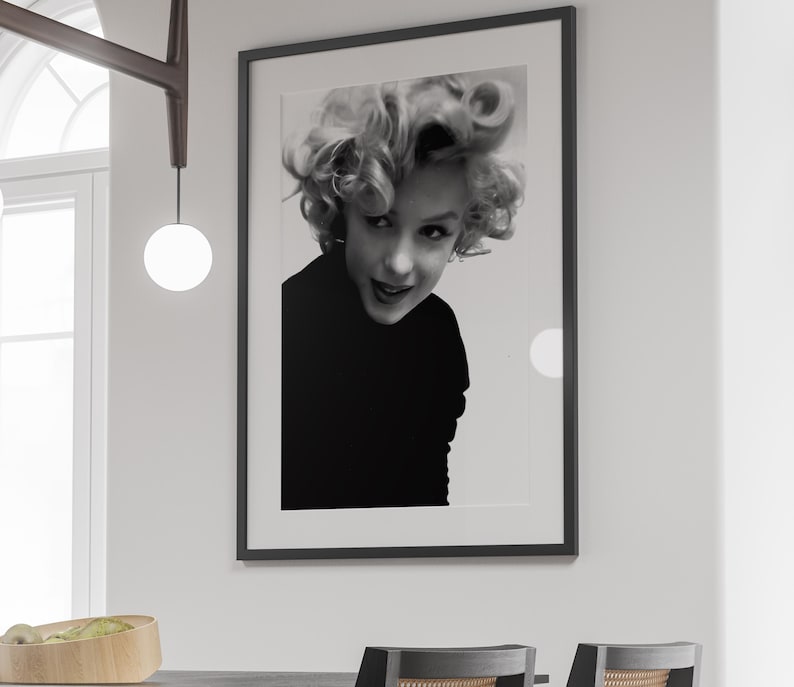 Peut inclure: Photographie en noir et blanc d'une femme aux cheveux courts et boucl&eacute;s. Elle regarde la cam&eacute;ra et sourit. La photo est encadr&eacute;e dans un cadre noir.