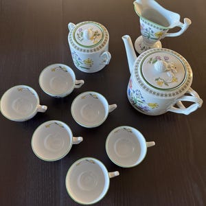 May include: A white tea set with floral designs. The set includes a teapot, creamer, sugar bowl, and six teacups.