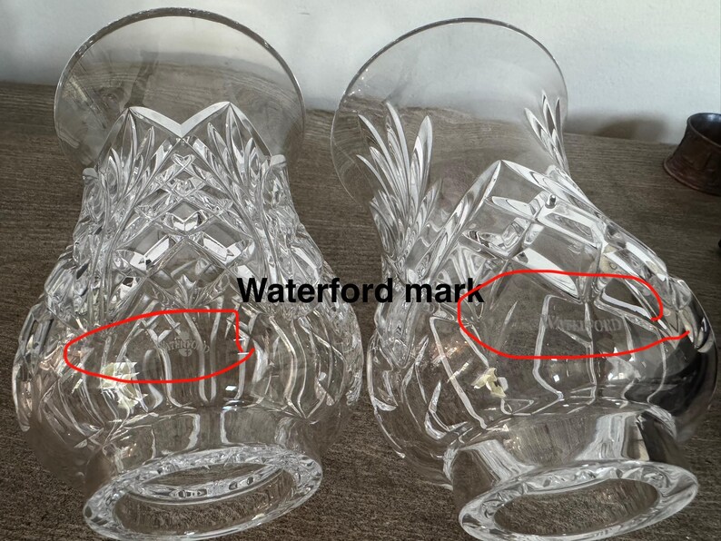 May include: Two clear crystal vases with diamond-cut patterns. The vases have a wide base and a flared top. The word "Waterford" is etched on the side of each vase. These decorative vases are ideal for displaying flowers.