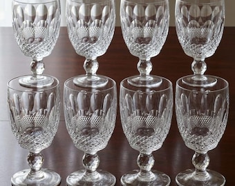 May include: A set of eight clear crystal wine glasses arranged in two rows of four. Each glass features a faceted stem, a round base, and a bowl decorated with a cut diamond pattern on the lower half and vertical oval arches on the upper half.