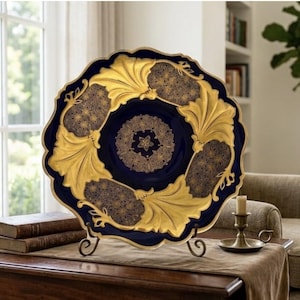 May include: A decorative plate featuring a deep navy blue base with intricate gold leaf patterns. The design includes large, embossed gold floral motifs alternating with detailed filigree sections, all set within a scalloped, gold-trimmed edge.