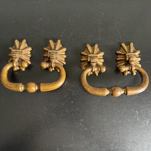 May include: Four antique wooden drawer pulls. Each pull features a decorative, sunburst-like design at the top and a curved handle. The pulls are a warm, medium brown color, suggesting they are made of wood.