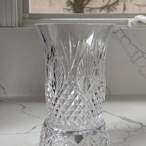 May include: A clear crystal vase with a cut glass design. The vase has a round base and a flared top. The vase is made by Waterford Crystal.