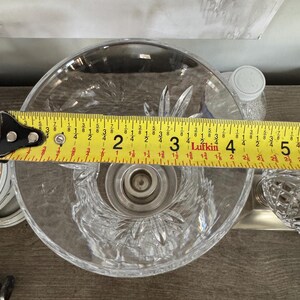 May include: A clear, cut-glass bowl with a central candle holder. The bowl is approximately 4 inches in diameter. The design features a starburst pattern. A measuring tape is placed across the bowl.