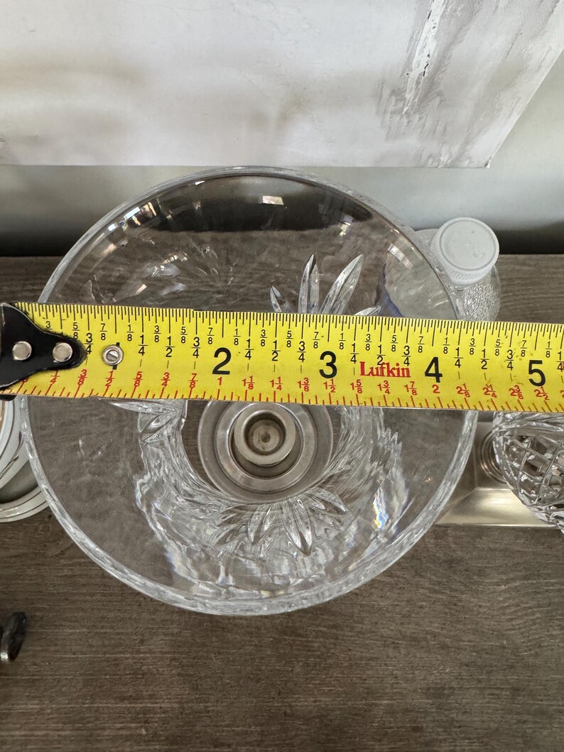 May include: A clear, cut-glass bowl with a central candle holder. The bowl is approximately 4 inches in diameter. The design features a starburst pattern. A measuring tape is placed across the bowl.