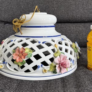 May include: White porcelain ceiling light fixture with a lattice design and floral accents. The fixture has a blue and white trim and is decorated with pink, red, and yellow flowers.