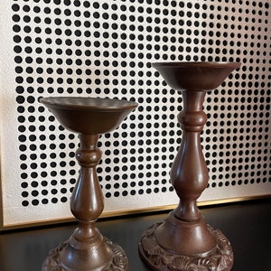 Puede incluir: Dos candelabros de metal marrón con un diseño decorativo. Los candelabros están sobre una superficie oscura.