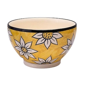Puede incluir: Un cuenco de cerámica con exterior amarillo adornado con motivos florales blancos. El borde es negro y el interior es color crema. El cuenco tiene forma redonda y una base sólida, adecuado para servir alimentos o como pieza decorativa.