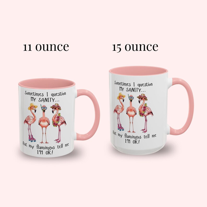 May include: Two white ceramic mugs with pink handles and interiors. Each mug features a flamingo design with the text "Sometimes I question my sanity... But my flamingos tell me I'm OK!" The mugs are labeled "11 ounce" and "15 ounce".