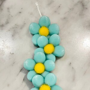 Puede incluir: Una vela en forma de flor azul y amarilla. La vela está hecha de cera y tiene un centro amarillo con una capa exterior azul. La vela tiene forma de flor con cinco pétalos.