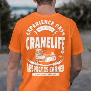 May include: Orange t-shirt with a white graphic design featuring a crane, the text "EXPERIENCE PAYS", "HEAVY LIFT SPECIALIST", "CRANELIFE", "1988", "RESPECT IS EARNED", and "IF YOU DONT GRIND - YOU DONT SHINE".