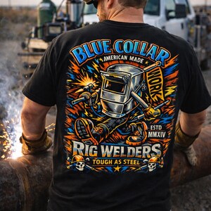 May include: Black t-shirt with a colorful graphic of a welding character, the words "Blue Collar American Made" and "Rig Welders Tough as Steel" are displayed. The shirt is worn by a person wearing a welding helmet.