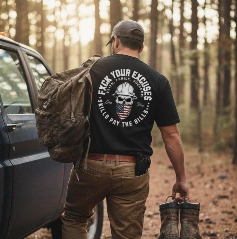 May include: A black t-shirt with a circular graphic on the back featuring a skull wearing a hard hat and an American flag bandana. The text reads "F*ck Your Excuses" and "Skills Pay the Bills". The person is wearing brown pants and a gray cap.