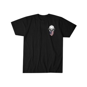 May include: Black t-shirt featuring a graphic of a skull wearing a white hard hat and an American flag bandana. The design is on the left chest area of the shirt. The t-shirt has short sleeves and a crew neck.