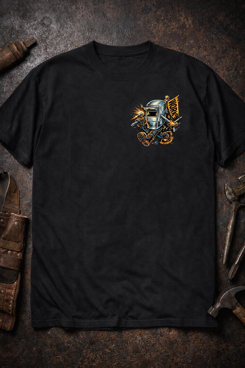 May include: Black t-shirt featuring a cartoon welder with a welding mask, holding a torch, and a flag that says "WORK". The graphic is in shades of gray, orange, and yellow. The shirt is a crew neck.
