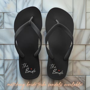May include: Two black flip-flops with the text "The Bride" in white script and a small red heart.