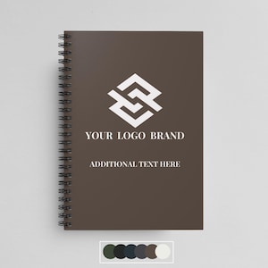 Peut inclure: Un carnet à spirales marron avec un logo géométrique blanc et le texte "YOUR LOGO BRAND" et "ADDITIONAL TEXT HERE".