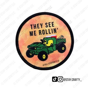 May include: Round patch with a black border featuring a green ATV illustration and the text "THEY SEE ME ROLLIN'". The background is a gradient of orange and yellow. The patch also includes the text "HTTPS://STAYCRAFTY.AT".