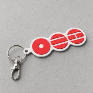 May include: A white keyring featuring three connected circular segments with red raised details. The first segment has a red ring, the second has three horizontal red bars, and the third has a red letter H. A silver metal split ring and lobster clasp are attached.