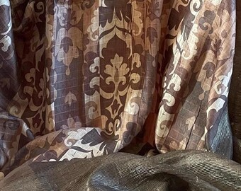May include: A brown and beige patterned fabric with a damask design. The fabric is folded and has a textured, woven look.