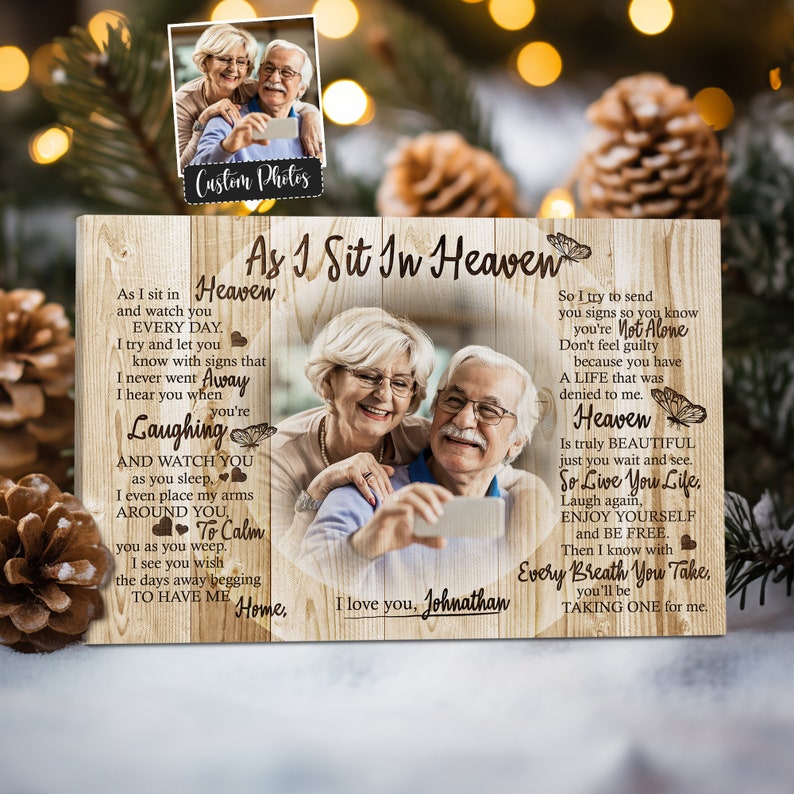 May include: A wooden sign with a heart shape in the center. The sign has a light wood background with a darker wood grain pattern. The sign features a photo of an older couple smiling and taking a selfie. The text on the sign reads "As I Sit In Heaven" and includes a poem about love, loss, and remembering a loved one.