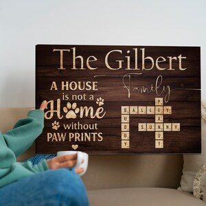 May include: A wooden sign with the words "The Gilbert Family" in a decorative font. The sign includes the phrase "A house is not a home without paw prints" and a crossword puzzle with family names.