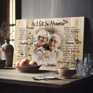 May include: A wooden sign with a photo of an older couple smiling and holding a phone. The sign has a poem about heaven and the text "As I Sit In Heaven" at the top.