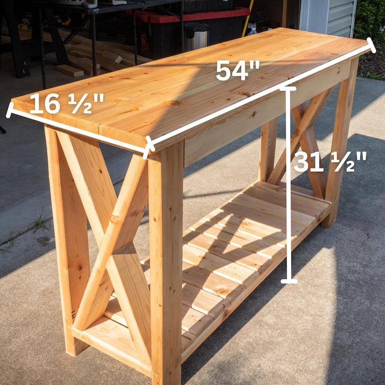 May include: A natural wood console table with an X-shaped support design. The table is 54 inches long, 16 1/2 inches wide, and 31 1/2 inches tall. It features a lower shelf for storage and is constructed from light-colored wood.