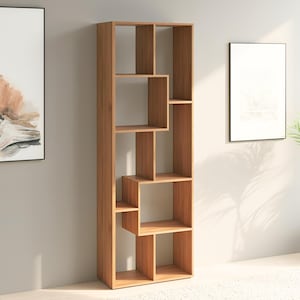 Könnte beinhalten: Ein hoher, hellbrauner Bücherregal aus Holz mit asymmetrischem Design. Das Bücherregal verfügt über unterschiedlich große offene Fächer und Regale, ideal zum Präsentieren von Büchern und Dekoration. Das Regal steht vertikal an einer neutralen Wand.