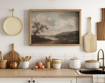 May include: A framed landscape painting of a river scene with trees and hills. The painting is hanging on a white tiled wall in a kitchen with wooden cutting boards, a copper pot, and white ceramic canisters.