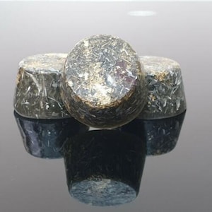 May include: Three cylindrical, dark gray objects with a metallic, textured appearance. The tops of the cylinders are rounded, and the surfaces reflect light, creating a shimmering effect. The objects are arranged closely together, with their reflections visible below.