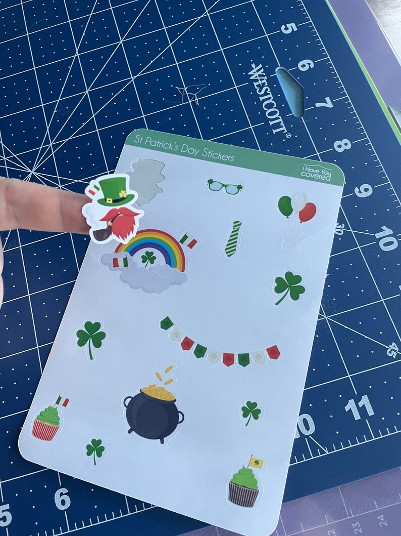 May include: A sheet of St. Patrick's Day stickers featuring a leprechaun, rainbow, shamrocks, a pot of gold, cupcakes, and other festive designs. The stickers are on a white background.