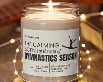 May include: A brown soy wax candle with a white label that reads "The Calming Scent of the end of Gymnastics Season". The label also includes the text "Organic, Non-Toxic" and "Infused with long practices and hard work".