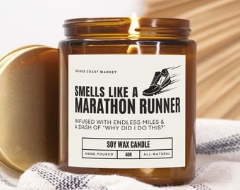May include: A brown glass candle jar with a gold lid. The label reads "Smells Like a Marathon Runner" with the text "Infused with endless miles & a dash of "Why did I do this?" Soy Wax Candle, Hand Poured, 40H, All-Natural."