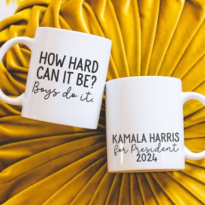 May include: Two white ceramic mugs with black text. The first mug says "HOW HARD CAN IT BE? Boys do it." The second mug says "KAMALA HARRIS for President 2024".