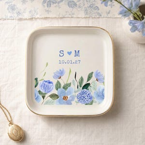 May include: A square ceramic trinket dish with a gold-toned rim, featuring a watercolor floral design in shades of blue and green. The center displays the letters S and M separated by a blue heart, with the date 10.01.27 printed below in blue.